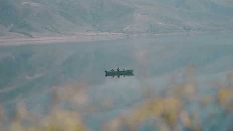 Tres-Pescadores-En-Un-Barco-Pescando-En-Una-Laguna-De-Agua-Cristalina-Con-Montañas-Al-Fondo