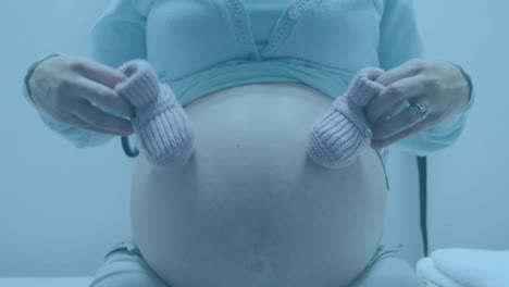 Fast-moving-clock-over-midsection-of-pregnant-caucasian-woman-holding-bootees-beside-belly