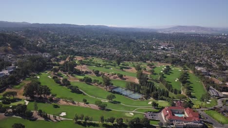 aerial helicopter shot of golf course field with mountains in background on a sunny day with clear blue sky rotate right 4k