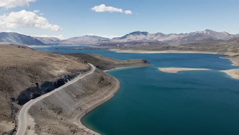 Backward-aerial-view-of-the-maule-lagoon-at-the-pehuenche-border-crossing-between-chile-and-argentina-on-a-sunny-day-with-the-andes-mountains-in-the-background