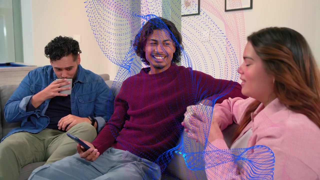 Tres amigos sentados en un sofá, la persona del centro mostrando el teléfono para entretenimiento, con una cinta azul flotando.