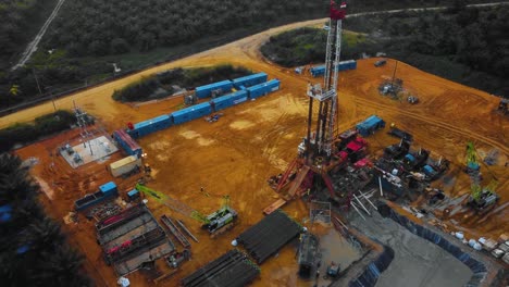 Cinematic-Drone-Footage-of-Onshore-Drilling-Rig-equipment-structure-for-oil-exploration-and-exploitation-in-the-middle-of-jungle-surrounded-by-palm-oil-trees-during-sunset-and-high-oil-price