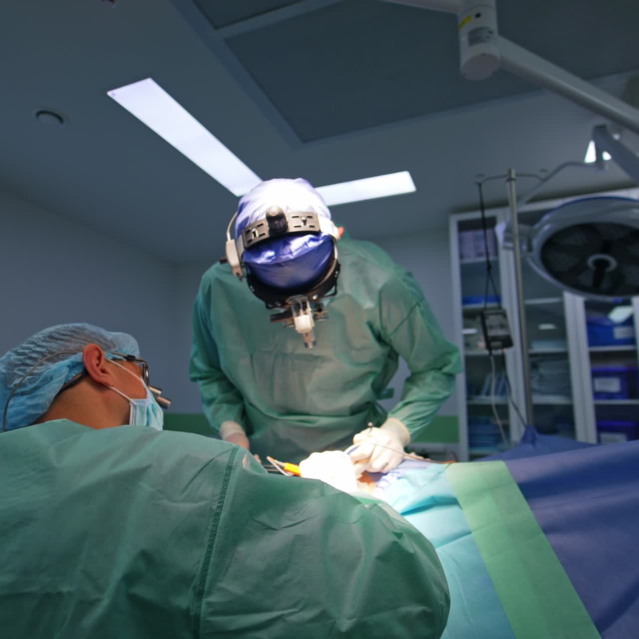Neurosurgeons cooperate at operation in modern hospital. Nurse at backdrop arranging instruments for surgery