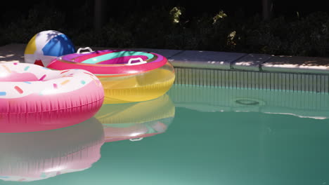 colorful pool floats and beach ball floating in sunny backyard pool