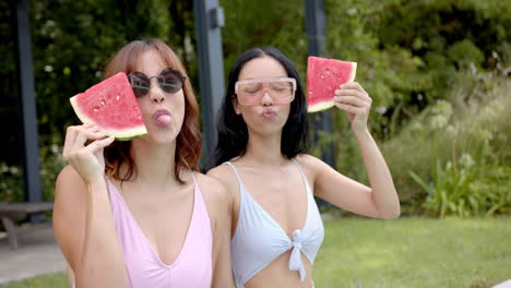 two young biracial female friends enjoy watermelon slices outdoors