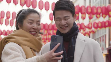 Joven-Pareja-Asiática-De-Vacaciones-Posando-Para-Selfie-En-Teléfono-Móvil-En-Chinatown,-Londres,-Reino-Unido-6