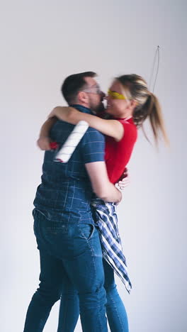 adorable young couple with transparent foil sheet and paint roller hugs and kisses at construction in empty renewing room