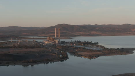 aerial: drone circling to the left around a power plant station next to a lake in new south wales, australia