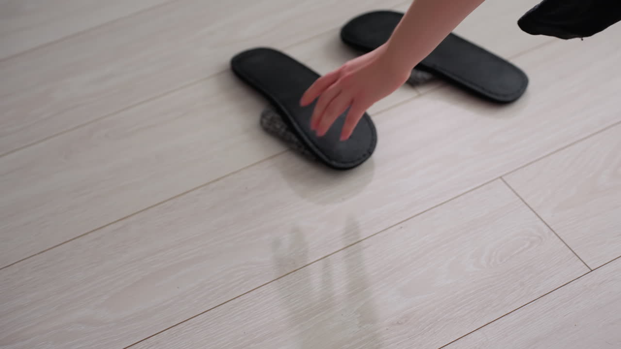 Close up of lady hand picking scattered clothes from floor dropping them on couch then preparing to carry slippers showing household tidying cleaning routine daily responsibility