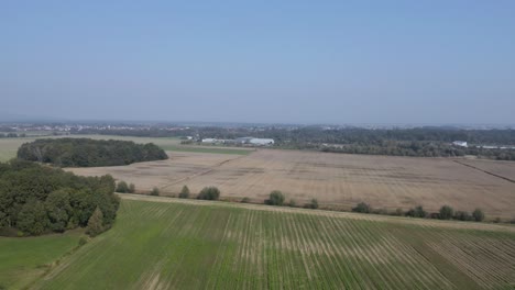 aerial view flying over cultivated farmland with the village of cresnjevec, slovenia, in the distance