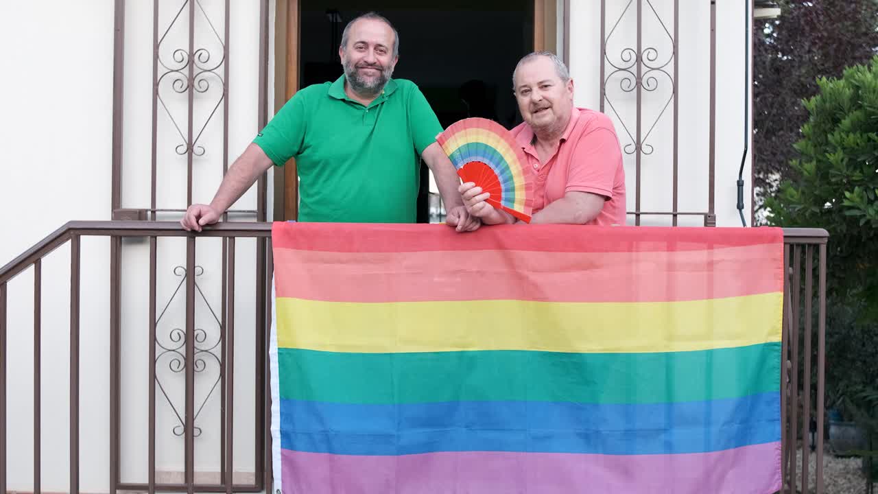 Two men on a balcony with a rainbow flag