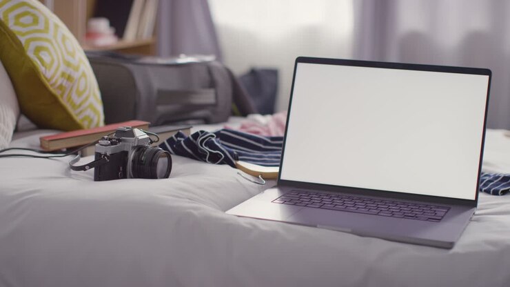Ordinateur portable à écran vide avec une valise ouverte sur le lit à la maison en cours de préparation pour les vacances d'été 1