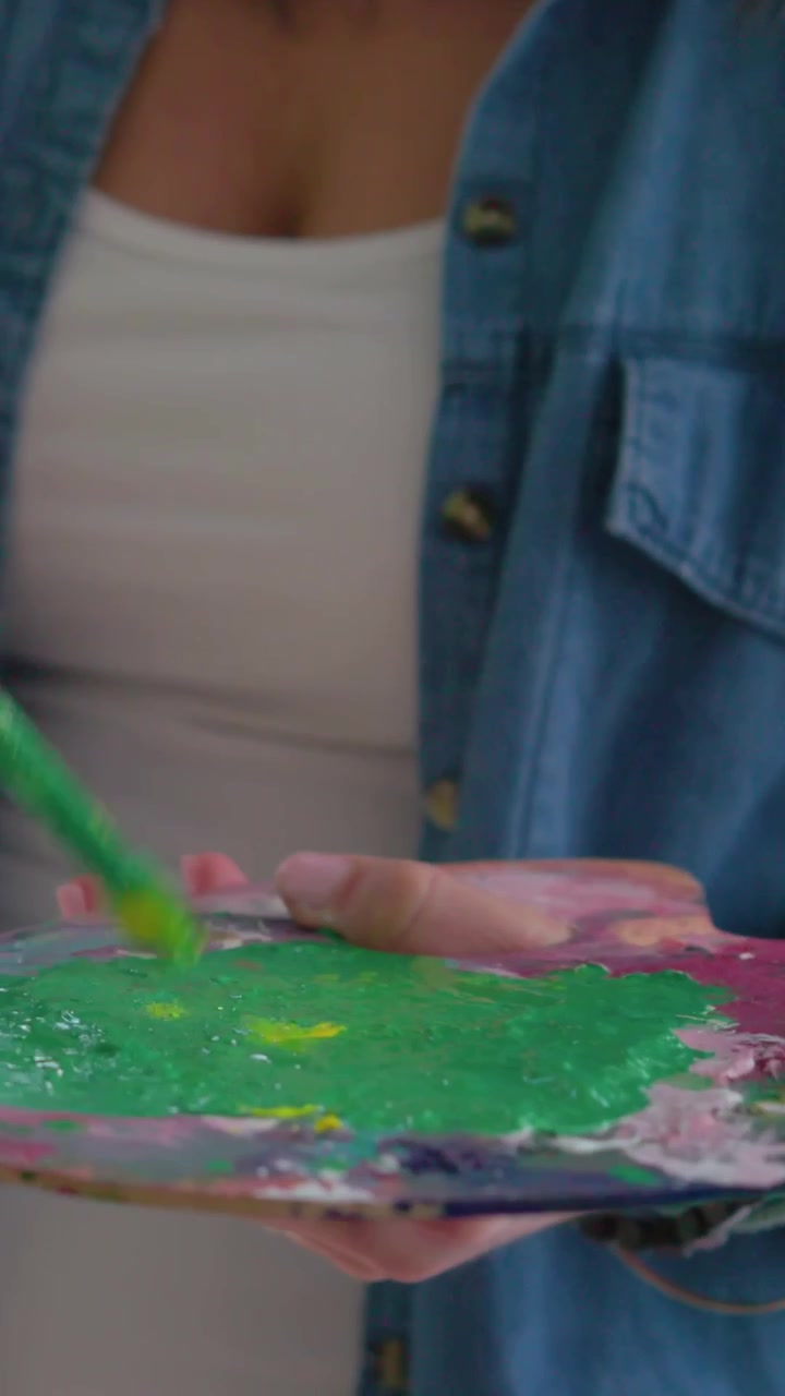Vídeo vertical: Pincel misturando, artista de jeans carregando tinta verde na paleta para pintar.
