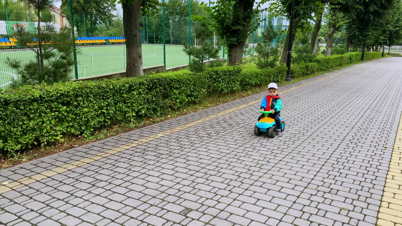 Little boy in cap approaching the camera on toy car. Toddler rides quickly pushing from the ground in the park.