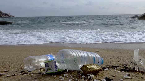 Botellas-De-Plástico-Llenas-De-Basura-En-La-Playa-Cerca-De-Una-Ola-Que-Corre,-Zoom-Lento-En-Toma-Constante