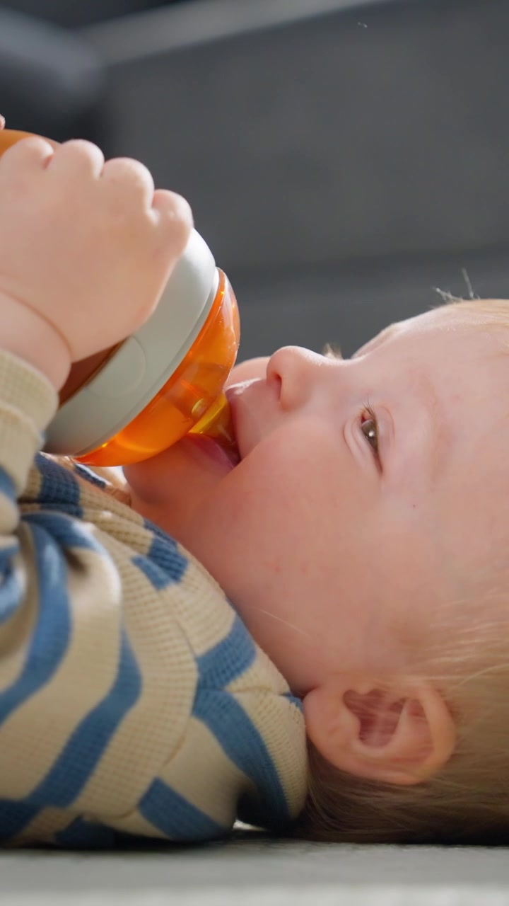 Bambino sdraiato che beve da un bicchiere con beccuccio