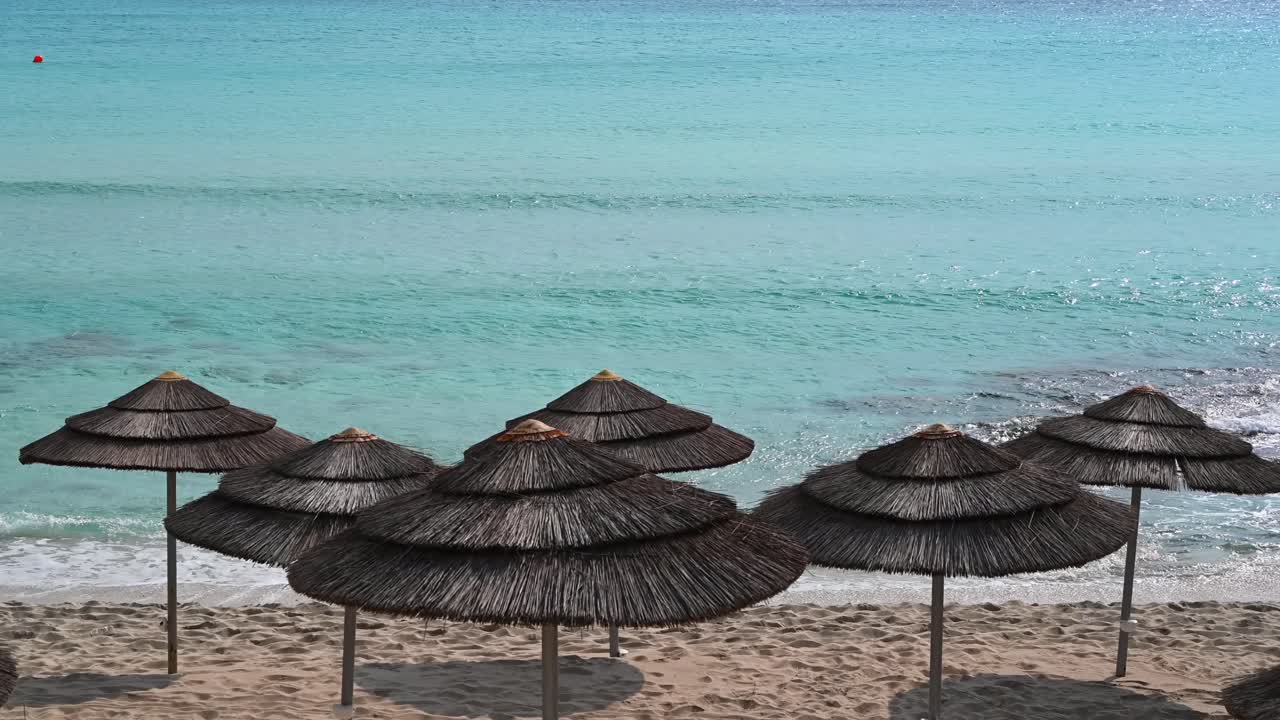 Straw beach umbrellas on the sand facing the turquoise Mediterranean Sea on the coast of Limassol, Cyprus
