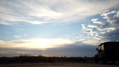 sliding motion time lapse with the silhouette of a jeep in the foreground as the sunset clouds roll across the sky over the mojave desert