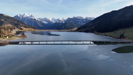 alpine landscape with steinbach viaduct over partially frozen lake sihl, euthal, clear day, aerial view