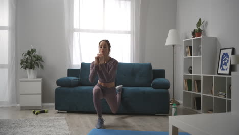 sexy slender woman is doing physical exercise at home at morning time squatting on one leg in living room sporty lady in interior of apartment