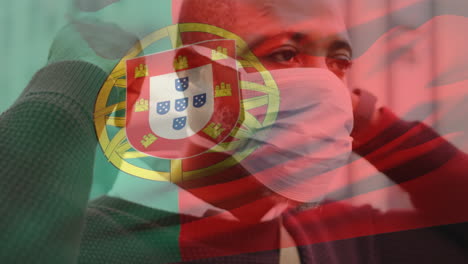 animation of flag of portugal waving over african american man wearing face mask in city street