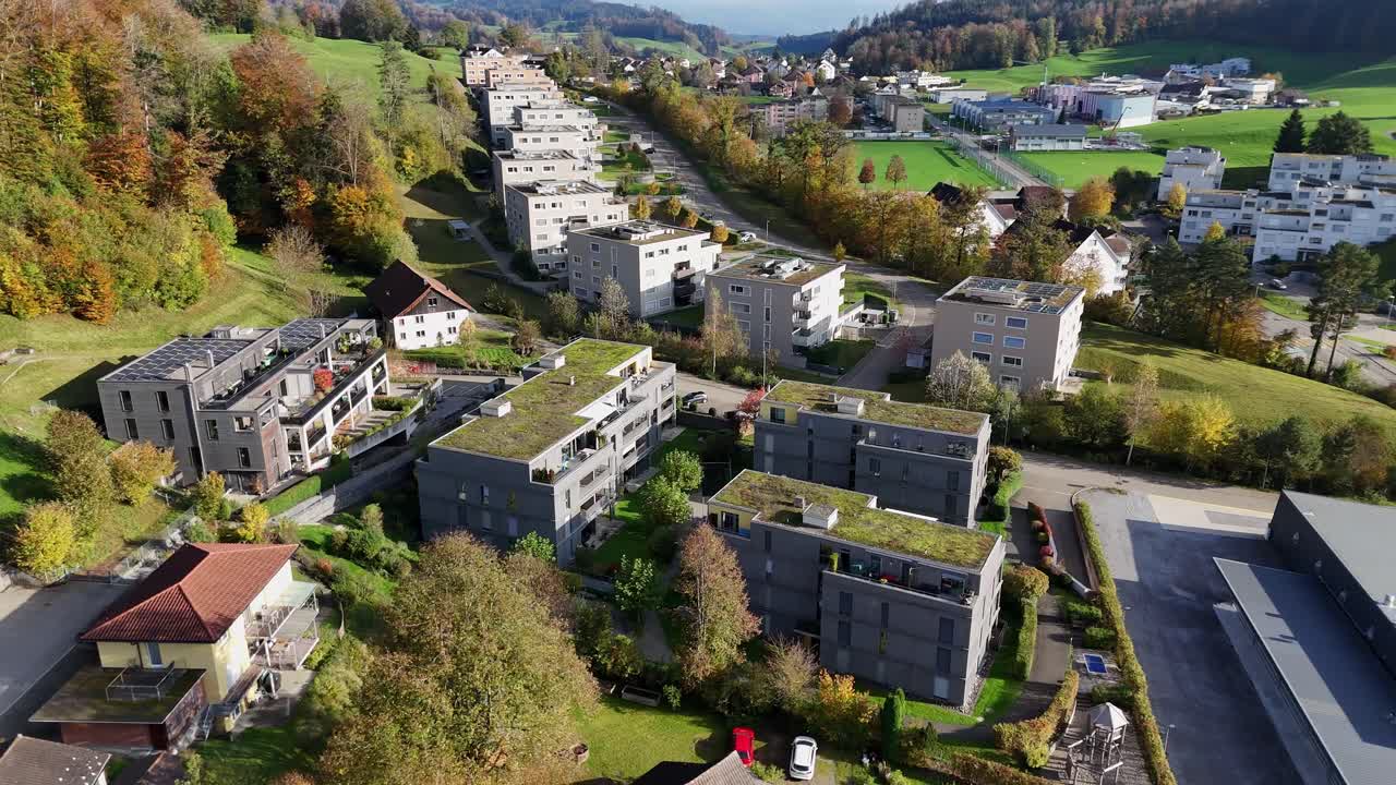 Aerial orbit shot of modern houses and Apartments with solar panels on roof. Green garden on rooftop of luxury homes in Swiss City. Beautiful autumn day wig colorful trees.