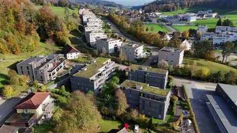 aerial orbit shot of modern houses and apartments with solar panels on roof. green garden on rooftop of luxury homes in swiss city. beautiful autumn day wig colorful trees.