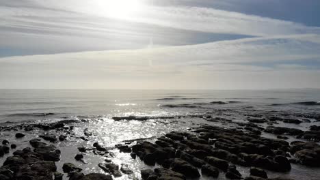 vuelo bajo aéreo sobre la silueta de las rocas con olas rompiendo suavemente en un día soleado y brillante