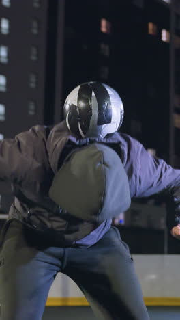 el deportista lanza hábilmente la pelota, la equilibra en la espalda, la empuja hacia arriba y la atrapa durante la práctica nocturna en un campo rodeado de edificios residenciales iluminados y farolas brillantes