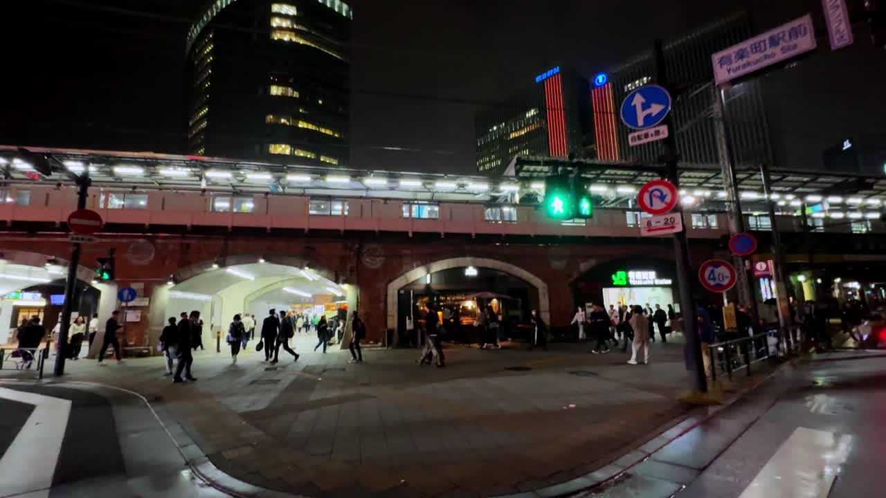 Night street scene in Tokyo with people crossing, tall buildings, and bright city lights
