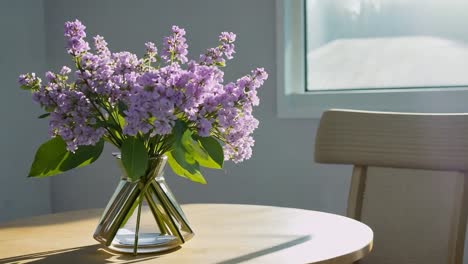 purple flowers in a vase on a table by a window