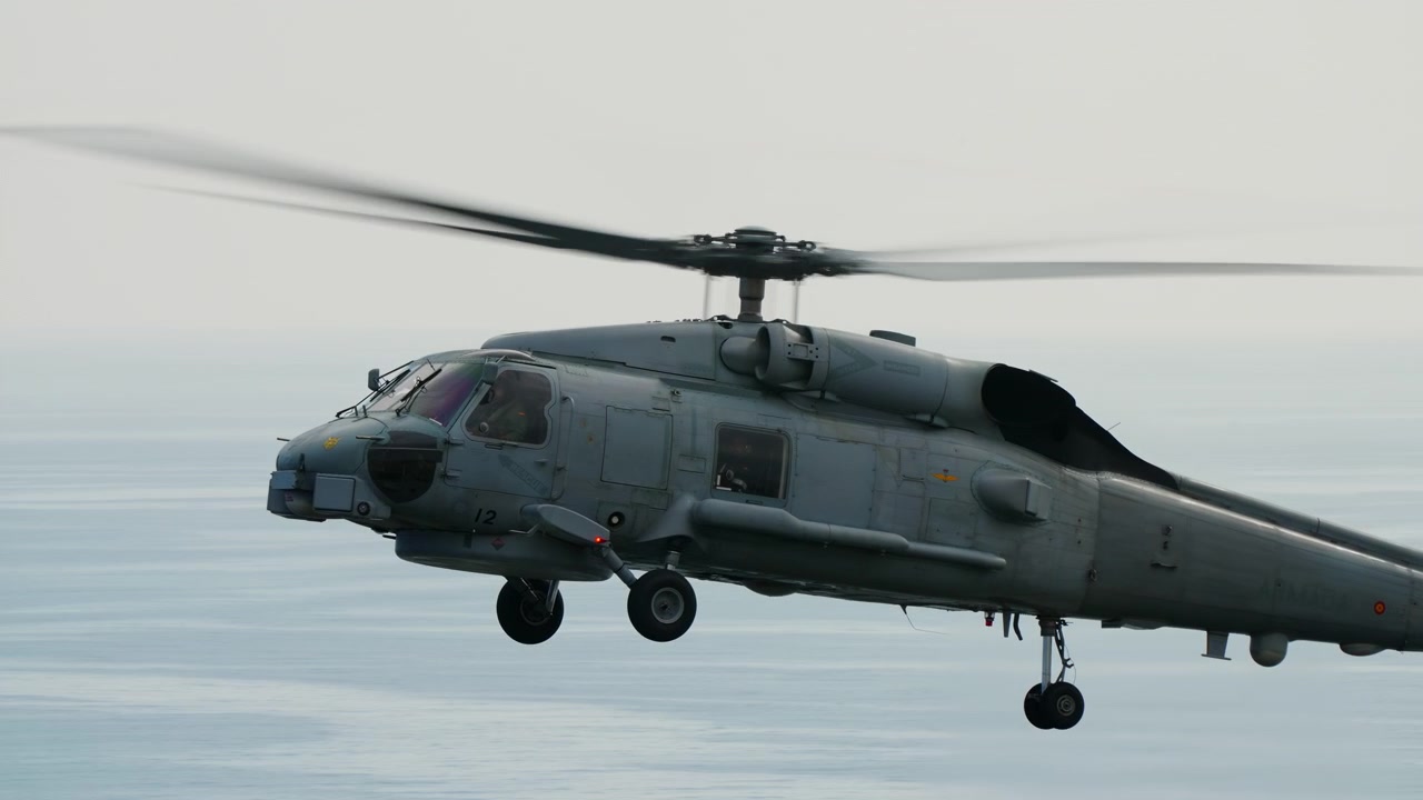 Military helicopter flying low over coastal water in overcast conditions