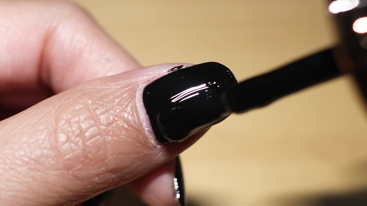 Detailed view of applying black nail polish on a fingernail with precision and care.