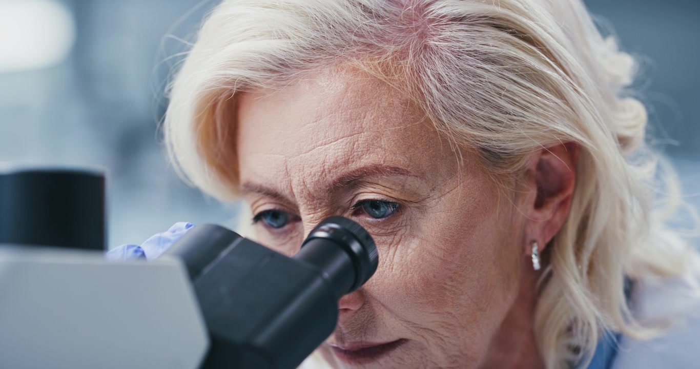 Scienziata anziana che esamina campioni al microscopio in laboratorio