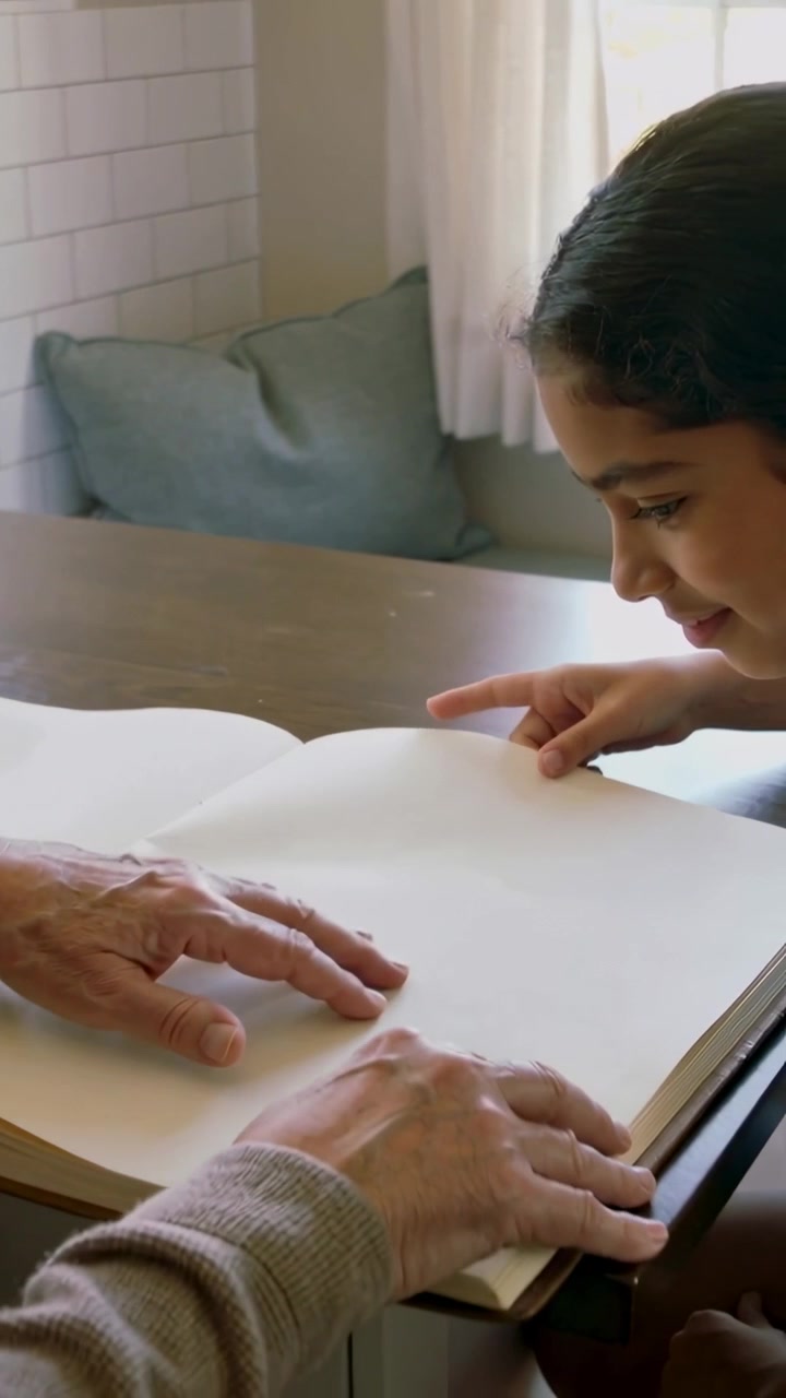 Vertical video: Lifting page corner older hands in sweater turning book at kitchen, guiding child