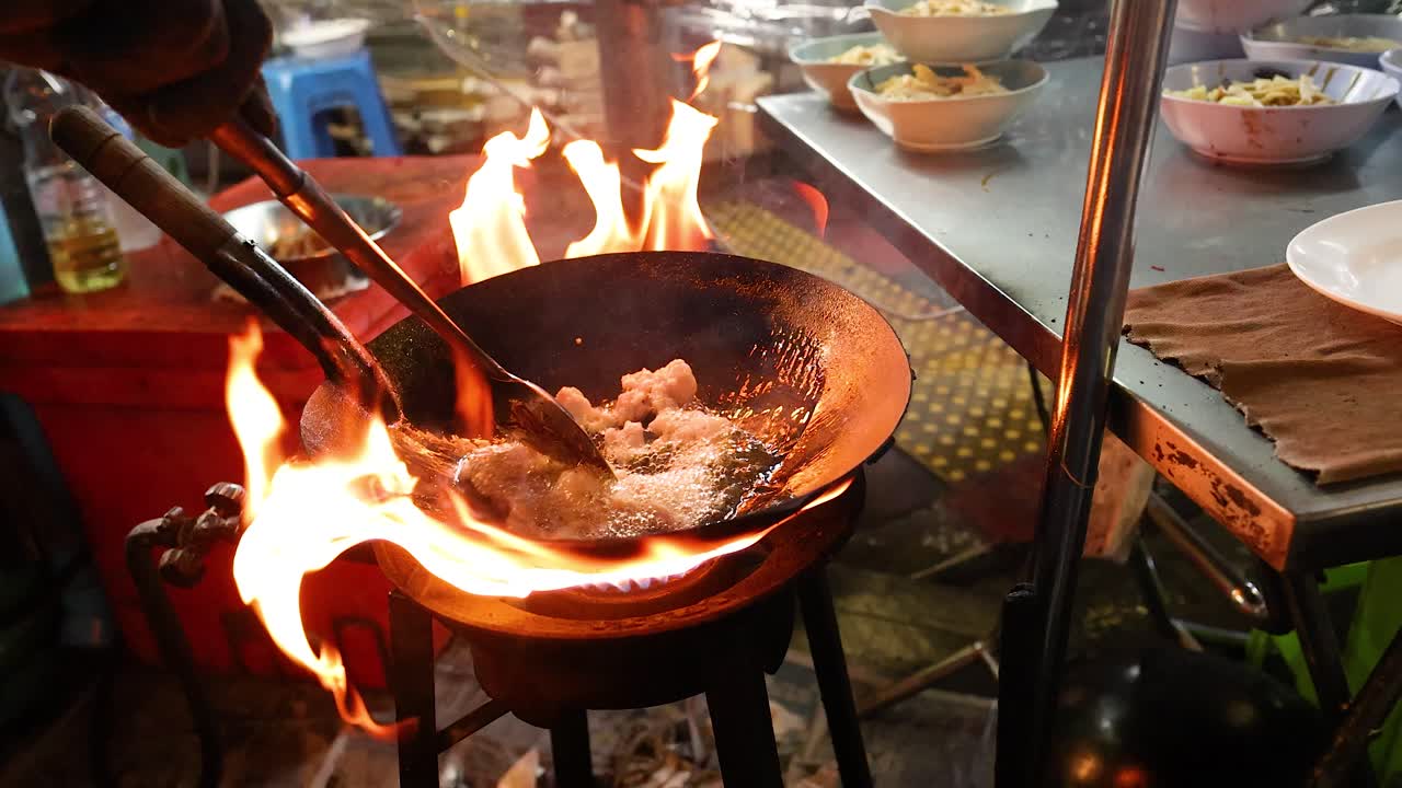 Chef stir-fries meat in flaming wok at night market, vibrant lighting, handheld camera, energetic mood