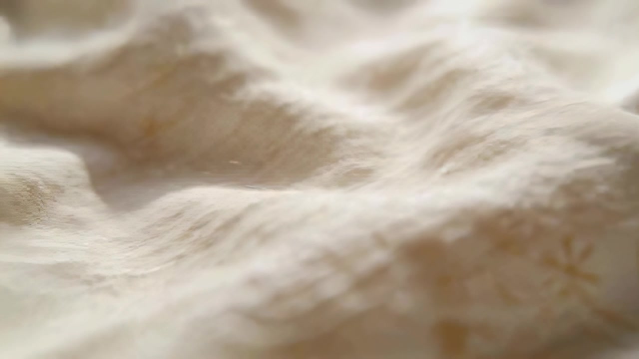 Camera shifting focus across cream wrinkled sheet in bedroom, showing pale floral lower-right