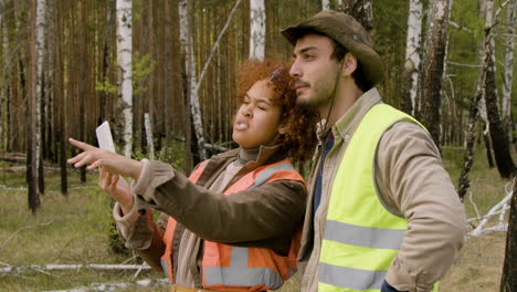 caucasian man and african american woman activists watching something in a tablet and deciding where to plant the trees