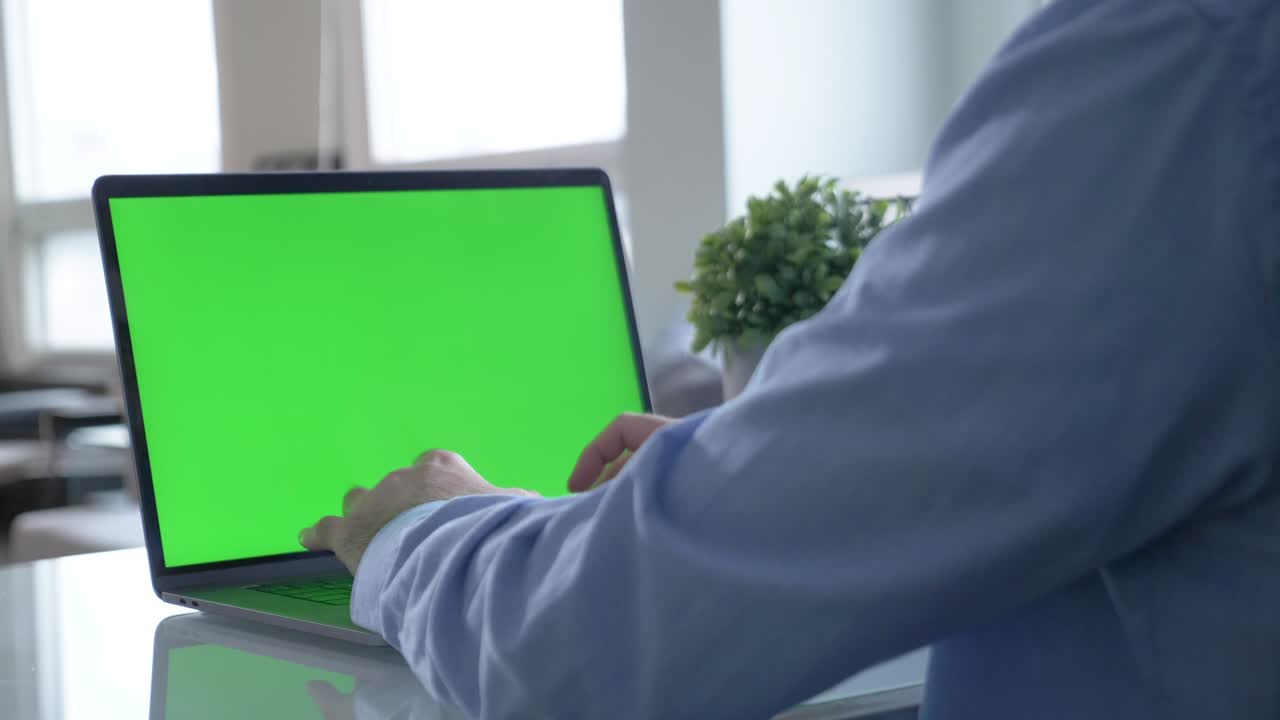 vista desde la parte de atrás de un hombre con camisa negra sentado en la mesa y escribiendo en una computadora portátil con pantalla de tecla de croma verde. imágenes de stock. laptop nuevo concepto de tecnología, pantalla verde de clave de croma