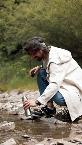 man filling water bottle in a mountain stream