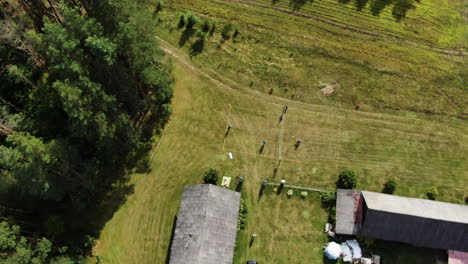 Grupo-De-Personas-Juega-Voleibol-En-Una-Antigua-Granja-Recreativa-Con-Hierba-Verde,-Vista-De-órbita-Aérea