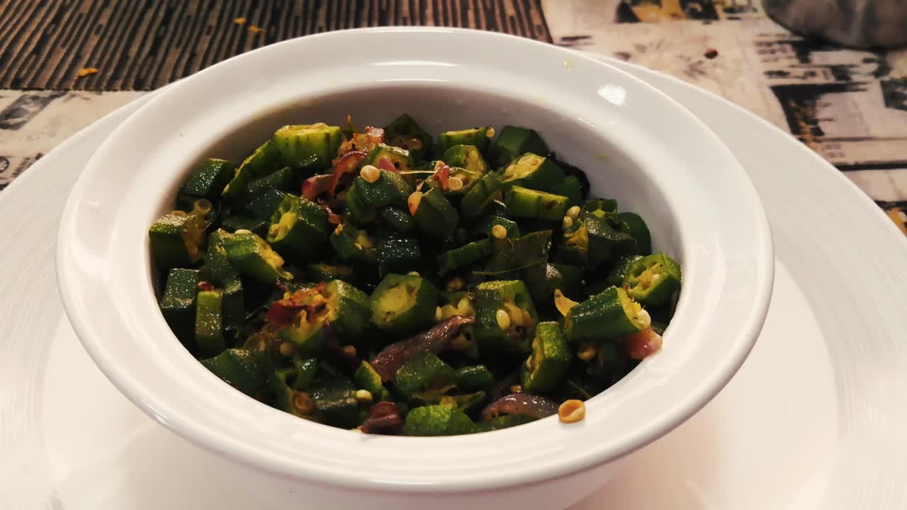 Using a spoon to take Stir fried okra from white ceramic bowl