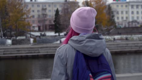 woman with backpack walking along a river in a city during winter