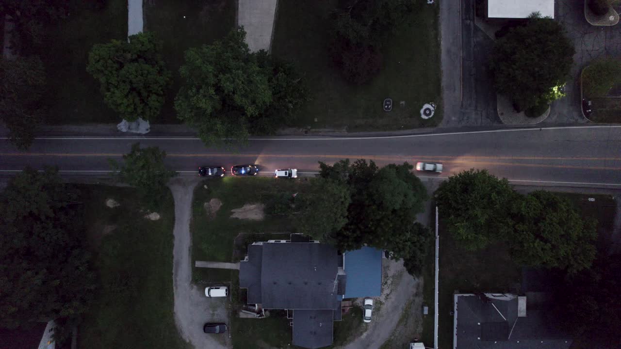 High-quality overhead drone footage capturing a dramatic scene where a car is pulled over by two police cars on a roadway