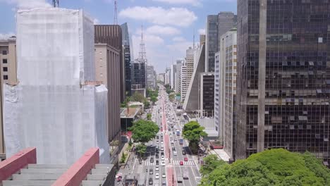 Sao-Paulos's-and-Brazil's-main-street-Avenida-Paulista-on-a-busy-crowded-sunny-day-full-of-traffic-and-people--slow-aerial-drone-shot-of-buildings-and-road