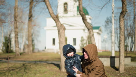 a close-up of a son and father holding hands, the child, dressed in a shiny black jacket, is pointing at something with excitement, while the father playfully carried him as he squat