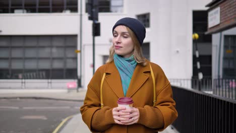 Busy-professional-young-Caucasian-woman-walking-down-a-London-street-with-a-cup-of-coffee-in-her-hands-and-looking-around