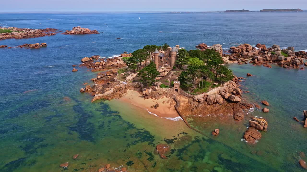 Drone orbiting Château de Costaérès on a rocky islet off Trégastel, surrounded by turquoise water and sailing boats - France