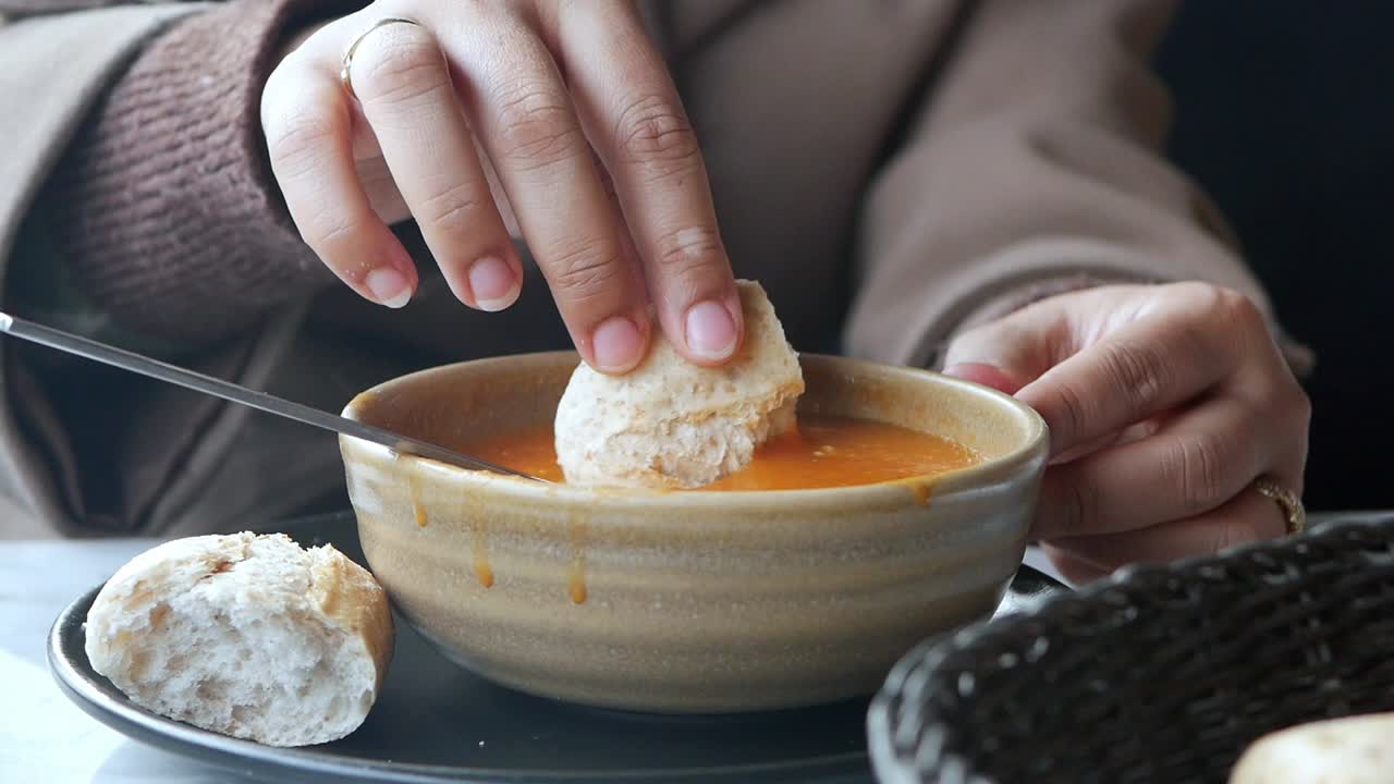 Primo piano di mani che intingono il pane in una ciotola calda di zuppa.