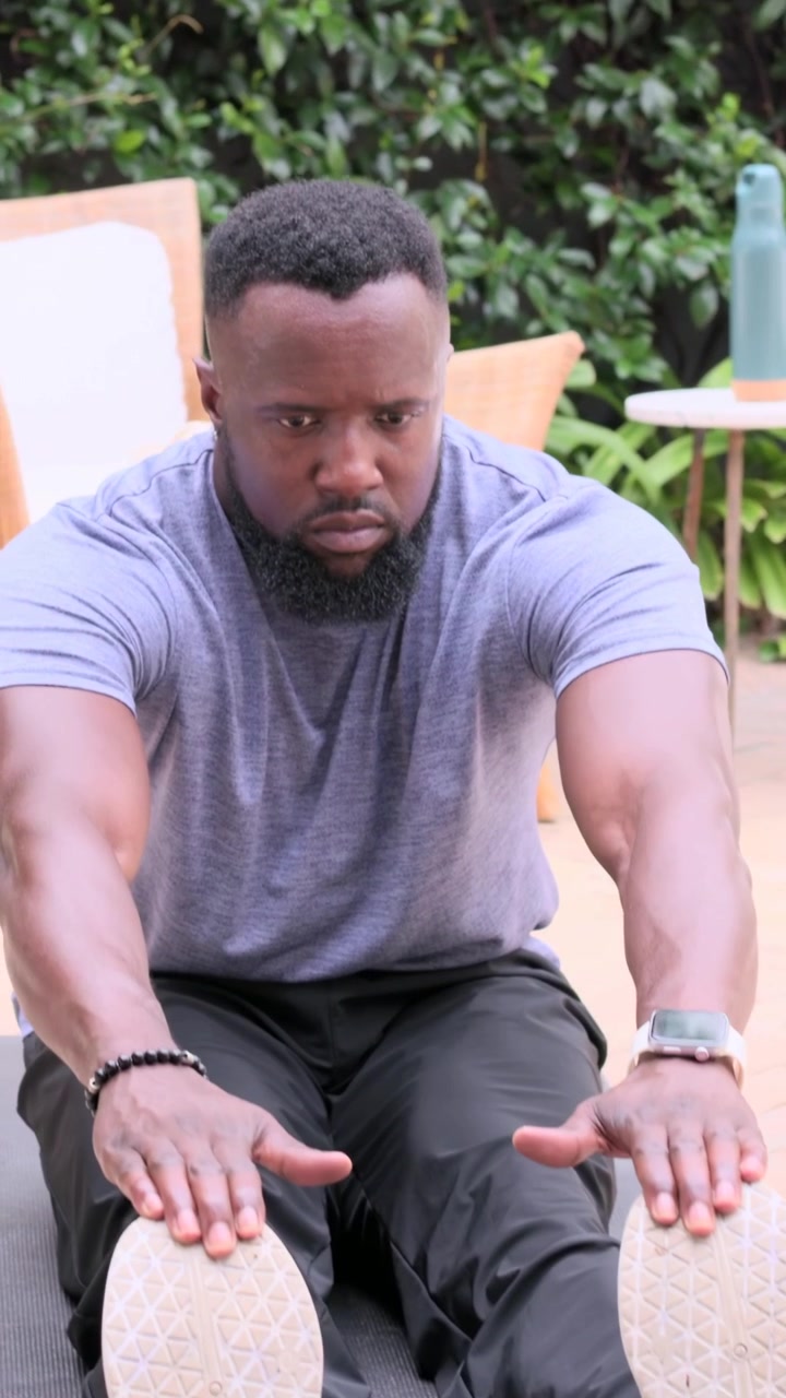 Vertical video: Starting mat stretch, man in gray shirt reaching then twisting on patio with bottle